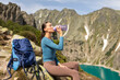 © Home-stock - Young lady with backpack drinking water, sitting with beautiful view in mountains and resting with water bottle during hike
