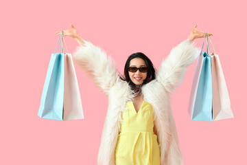 Sticker - Happy beautiful young Asian woman in sunglasses with shopping bags on pink background