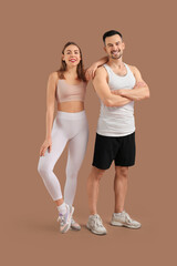 Wall Mural - Beautiful young happy couple in sportswear doing exercises on brown background