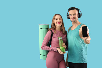 Canvas Print - Young happy couple in sportswear with bottle of water, yoga mat and mobile phone on blue background