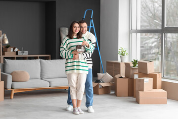 Wall Mural - Happy young couple with keys and house model in room on moving day