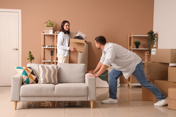 Poster - Happy young woman with her husband carrying sofa in room on moving day