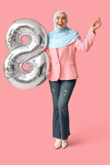 Wall Mural - Happy young Muslim woman in hijab with silver air balloon in shape of figure 8 on pink background. International Women's Day