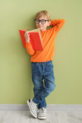 Poster - Cute little boy in eyeglasses with open book standing against color wall