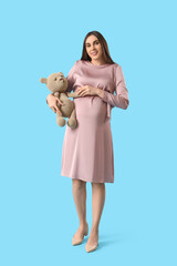 Sticker - Young pregnant woman with toy bear on blue background