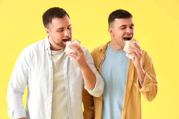 Canvas Print - Handsome young men eating tasty doner kebab on yellow background