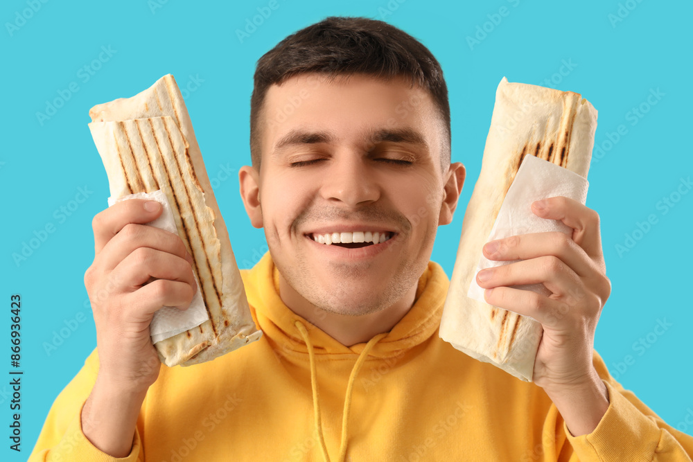 Handsome young man with tasty doner kebab on blue background