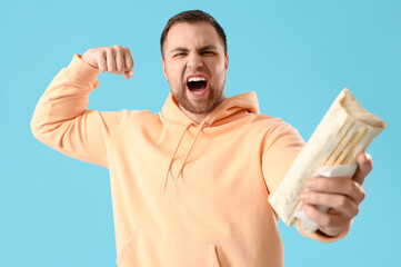 Sticker - Handsome young man with tasty doner kebab showing muscles on blue background