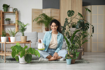 Wall Mural - Portrait of beautiful young African-American woman with watering can and plants in living room