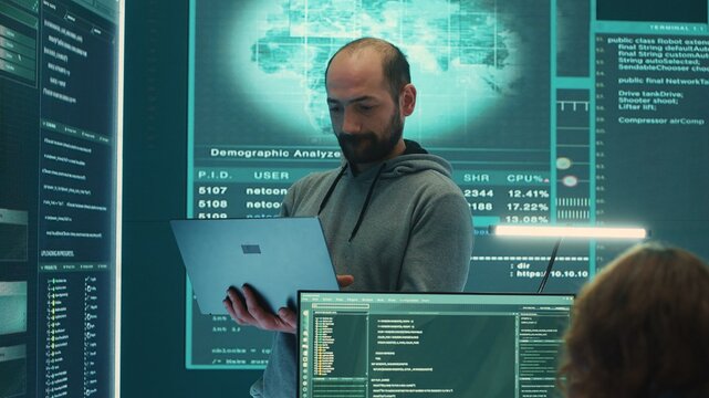 Governmental hacker examines info on a big screen in agency office, using advanced technology to secure computer networks. Working on cyber security and defending against cyberwarfare. Camera A.