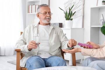 Wall Mural - Senior man with glass of water taking pill from caregiver in nursing home