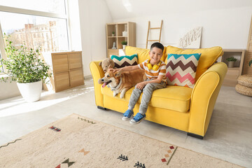 Wall Mural - Little happy Asian boy with cute Corgi dog in headphones sitting on sofa at home
