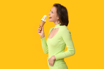 Wall Mural - Beautiful young woman with sweet ice-cream in waffle cone on yellow background
