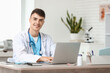 © Pixel-Shot - Young male doctor working with laptop at table in clinic