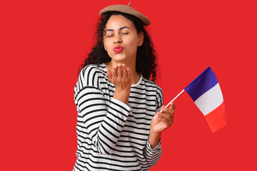 Wall Mural - Beautiful young African-American woman with flag of France blowing kiss on red background