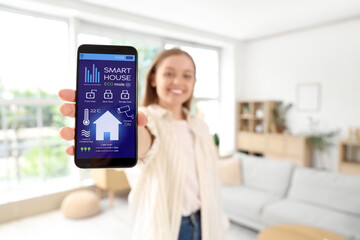 Canvas Print - Young woman holding mobile phone with smart home security system control panel in room, closeup