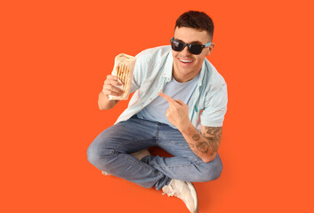 Canvas Print - Handsome young man pointing at tasty doner kebab and sitting on orange background