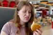 © Евгений Шемякин - Sad depressed young woman eating burger in fast food restaurant. Eating disorder concept.