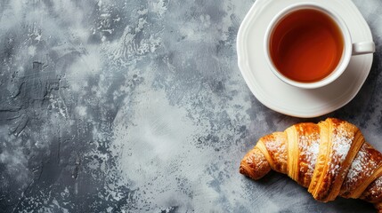 Wall Mural - Top view of a cup of tea and a tasty croissant with space for text