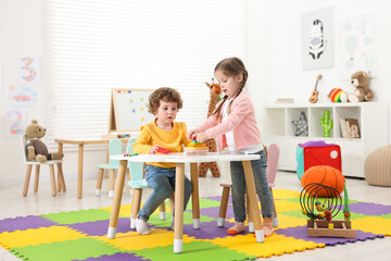 Wall Mural - Cute little children playing with colorful toy pyramid at white table in kindergarten