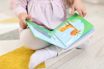 Wall Mural - Little girl with book on floor in kindergarten, closeup