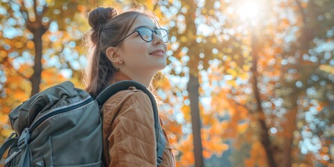 Wall Mural - A student girl with a backpack and glasses in the park in autumn