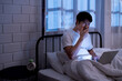 © MergeIdea - Asian tired man sitting in bed yawning while working overload on his laptop late at night in a dimly lit room before go to sleep