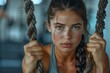 © Jane_S - Rear view of a woman with braided hair working out with battle ropes in a gym, showcasing her strength and dedication.