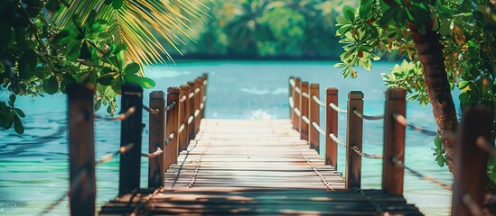 Wall Mural - Tranquil tropical landscape with a wooden pier leading to the blue and beautiful waters. This pier is surrounded by green trees which create a peaceful and calming atmosphere
