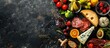 © Lasvu - Table with appetizers: cheese, fruits, and charcuterie on a dark background, viewed from above with space for text