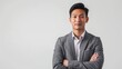 © liliyabatyrova - A confident Asian businessman stands with arms crossed against a white background. He is dressed in a grey suit and white shirt
