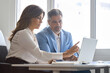 © insta_photos - Two busy mature professional business man and woman executives team using laptop working on computer having conversation on financial project in office. Bank manager consulting client at meeting.
