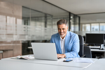 Wall Mural - Happy senior 50 years old professional business man wearing suit using computer sitting at desk. Busy smiling middle aged businessman executive investor bank manager working on computer in office.