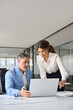 © insta_photos - Two busy professional executives company team working in corporate office using pc laptop. Professional mature business man and woman leaders colleagues talking working on computer at work desk.