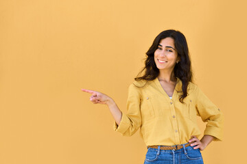 Wall Mural - Joyful young middle eastern woman showing at copy space for advertising on yellow background. Smiling Arabian or latin girl consumer, buyer in casual shirt pointing finger aside for recommend, promo