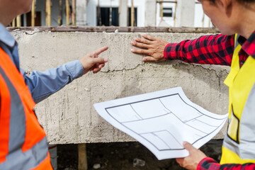 Wall Mural - Two male construction workers, including an Asian engineer, meticulously review structural plans and design concrete columns and beams for a new residential build.