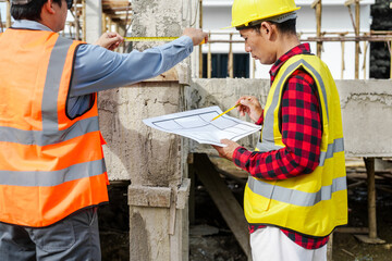 Wall Mural - Two male construction workers, including an Asian engineer, meticulously review structural plans and design concrete columns and beams for a new residential build.