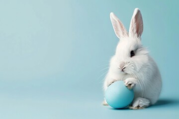 photo of a white cute fluffy bunny sitting on a blue easter egg isolated on a pastel background, copy space concept for Happy Easter or Springtime decoration