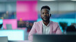 © NaphakStudio - African American male news anchor in a pink blazer sitting at a desk in a neon-lit studio, blending professional attire with a modern and colorful workspace.