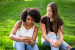 © Brocreative - How is social media affecting our teens? Concept photo of two teenage diverse girls sitting together looking at a smartphone and viewing social media content