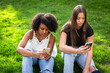 © Brocreative - Is social media making our teens less social? Concept photo of two teenage diverse girls sitting together on their phones and not talking to each other.