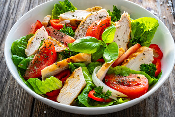 Poster - Caesar style salad - delicious grilled chicken breast slices and fresh vegetables and seasonings served in white bowl on wooden table
