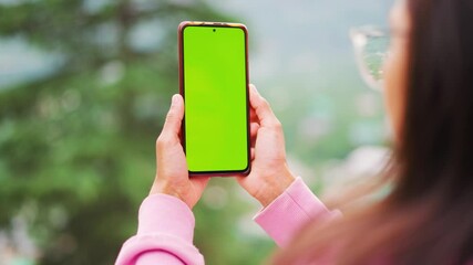 4K shot of woman holding phone in hand with green screen and standing outdoors. Chroma key mock-up on smartphone in hand. Girl Using Smartphone, Browsing Internet, Watching Video Content, Blogs.