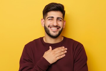 Wall Mural - A man with a beard smiles brightly while gesturing with his hand over his chest against a yellow background