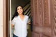 © AntonioDiaz - Latin woman happily opens the door to her new home, embodying the excitement of homeownership