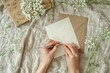 © qorqudlu - The image shows a person writing on a card, surrounded by delicate white flowers, set on a fabric background, creating a personal and heartfelt scene.