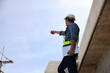 © naraichal - A smart Asian male engineer standing on a staircase concrete viaduct with an unfinished railway construction site. Moving forwards.