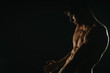 © qunica.com - Shirtless muscular young man posing in low light, showcasing his defined physique and strength. Dark and dramatic lighting creates a moody and intense atmosphere.