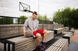 © Mihail - young basketball player sits on a wooden bench at an outdoor court, resting after a game. He is holding a basketball and looking off into the distance