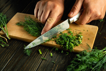Wall Mural - Chopping dill with a knife into a man hand to add to food before preparing a vegetarian dinner.